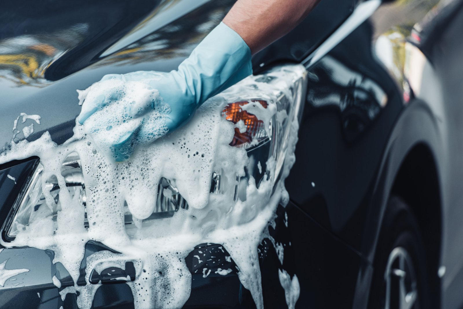 partial view of car cleaner washing car with sponge and detergent